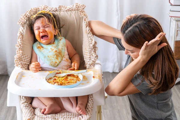 Yüzünde domates sosu olan mutsuz bir çocuk, annesi yanında otururken ağlıyordu. Dağınık küçük kız karışık ırk evde annemle spagetti yiyor..