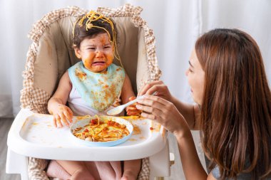 Yüzünde domates sosu olan mutsuz bir çocuk, annesi yanında otururken ağlıyordu. Dağınık küçük kız karışık ırk evde annemle spagetti yiyor..