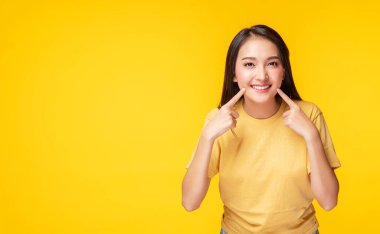 İzole edilmiş sarı arka planda dikilirken, parlak dişlerini işaret eden neşeli genç bir kadın. Temizlik dişlerini gösteriyor. Diş sağlığı ve sağlıklı konsept.