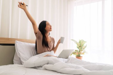 Yaşam tarzı teknolojisi ve çalışma iletişim konsepti. Serbest çalışan genç bir kadın, sabahları elinde kahve ya da çay tutarken dizüstü bilgisayarla sosyal uygulamaları kontrol ediyor..