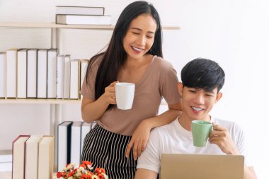 Yaşam tarzı karantina teknolojisi aile kavramı. Evde iş yerinde dizüstü bilgisayarla çalışırken elinde bir fincan kahve ya da çay tutan mutlu genç çift..