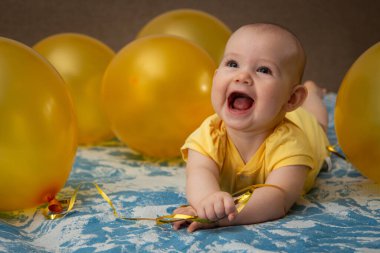 Sarı balonların ortasında sarı elbiseli küçük bir çocuk.