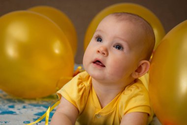 Sarı balonların ortasında sarı elbiseli küçük bir çocuk.