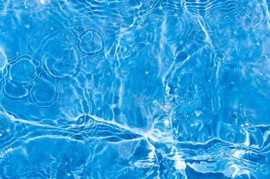 Yüzeydeki mavi su dalgaları bulanıklaştı. Defocus bulanık mavi şeffaf, berrak, durgun su yüzeyi dokusu sıçrama ve kabarcıklarla bulanıklaştırılmış. Parlak desenli arka planda su dalgaları.