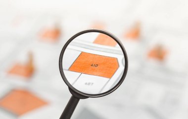 Kadastro haritasında büyüteç tutan adam arazi satın almak için değerlendirme arıyor. Satış, kira, alım, yatırım için inşaat ve konut inşaatı için boş araziyle emlak kavramı.