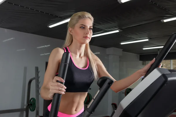 Athletic tanned blonde girl is at the gym. Doing the workout with a sexy sports costume. Running on the treadmill, legs pumping. The concept of a healthy lifestyle. — Zdjęcie stockowe