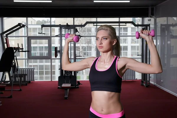 Athlete blonde is at the gym. Makes workout with a sexy sports costume. lifts weights, pumping the triceps. The concept of a healthy lifestyle. Royalty Free Φωτογραφίες Αρχείου