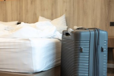 Büyük bir seyahat bavulu, yatağın yanında duruyor. Tertipli bir odada. Tatil ya da gidiş olabilir.