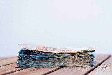 Tahta bir masanın üzerine yığılmış bir tomar banknot. 50 Euro 'luk banknot ve 20 Euro' luk banknot var..