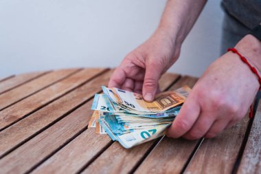Bir insan elleriyle bir masanın üzerindeki büyük banknotları topluyor. Bunlar, Avrupa Birliği 'nde kullanılan para birimi olan 50 ve 20 avroluk banknotlar..
