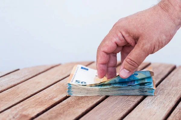 Tahta bir masadan almak istediği banknotları bir kişi seçiyor. Avrupa Topluluğunda kullanılan para birimi olan 50 ve 20 avroluk banknotlar görülebilir durumda