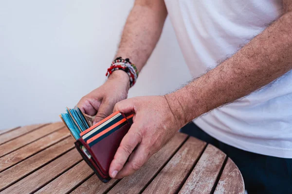 Bir adam kahverengi deri cüzdanına çok sayıda banknot doldurur. Tanımlanamayan birkaç kredi kartı var. Ameliyatı yıpranmış ahşap bir masada yapıyor..