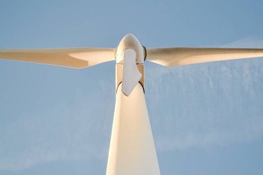 Aşağıdan, mavi bir gün gökyüzü ve bulutlarla renklendirilmiş elektrik yel değirmeni. Perspektif sahneyi daha da güçlendirir, çünkü yel değirmeninin bıçaklarından biri izleyicinin tam üstündedir.