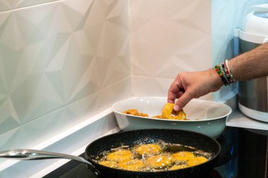 Bir adam yemek kasesinden taze yapılmış bir donut alıyor. Kendini zapt edemedi. Diğer çörekler kızartma tavasında yağda kızarıyor. Yakında yenmeye hazır olacaklar..