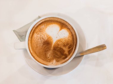 Zengin ve köpüklü Cafe con leche 'si olan beyaz bir fincanın Zenital görüntüsü. Birisi köpükle güzel bir kalp resmi çizmiş..