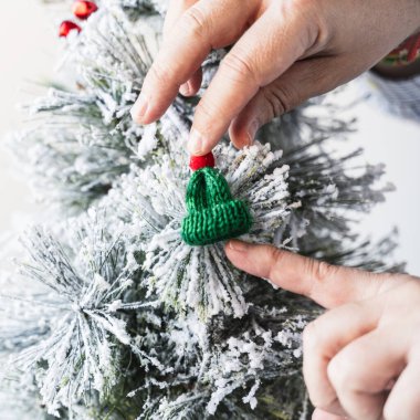 Bir insan, yapay Noel ağacında asılı küçük yeşil yün bir şapkanın minicik figürüyle oynuyor. Parmağını küçük şapkanın içine sokmaya çalışıyor..
