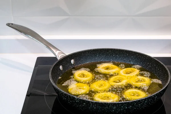 Beyaz bir mutfakta seramik bir tavada kızartma var. Tavada çok sayıda çöreğin kızardığı kızgın yağ var..