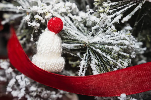 Beyaz yünden yapılmış minyatür bir kış şapkası. Tepesinde kırmızı bir top var. Plastik dallarında kar etkisi olan bir Noel ağacının dalına asılmış. Ren geyiği figürlü kırmızı bir kurdele ağacı sarıyor..