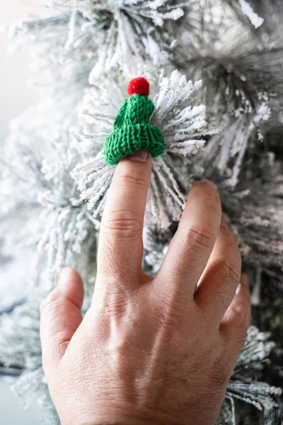 Birisi yapay Noel ağacına dekoratif bir figür olarak asılmış küçük yün bir bereyle oynuyor. Parmağını şapkanın içine soktu. Bu da şapkanın ne kadar küçük olduğunu gösteriyor..