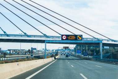 Çok şeritli bir otoyolda, yolun yukarısındaki metal bir yapının üzerinde aydınlık bir tabela var ve sürücülere sağ şeritten giriş olduğunu bildiriyor.