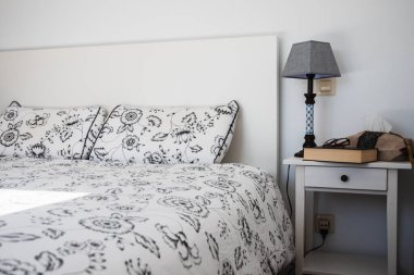 Siyah beyaz dekore edilmiş çift kişilik yataklı bir oda. Komodinin üzerinde bir kitap ve okuma gözlüğü var. Rahatlarken okuman için..