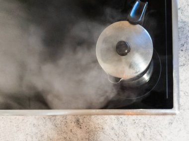 İtalyan kahve makinesi, kahve yapmak için suyun ısıtıldığı cam seramik hobın üzerine yerleştirilmiş. Kahve makinesinden buhar çıkıyor çünkü su kaynıyor. Boşluğu Kopyala