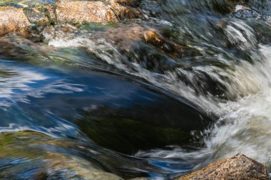 Küçük bir derede kayaların arasındaki şelaleyi görebilirsiniz. Suyun altında bitki örtüsü var.