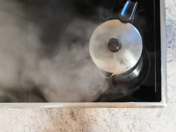 İtalyan kahve makinesi, kahve yapmak için suyun ısıtıldığı cam seramik hobın üzerine yerleştirilmiş. Kahve makinesinden buhar çıkıyor çünkü su kaynıyor. Boşluğu Kopyala