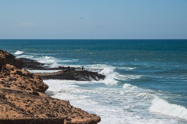 Fas bölgesinde Atlantik Okyanusu. Kıyıdaki kayalıklardaki bazı balıkçılar işlerini yaparken kayalara çarpan dalgalardan kaçıyorlar..