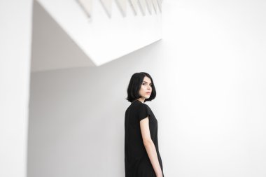 Sakin siyah saçlı kadın beyaz duvar karşı kamera arıyor