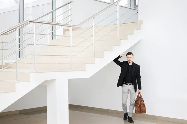Eleganter Mann mit Tasche in modernem Gebäude unter Treppenhaus Stockbild