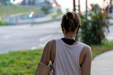Yazlık tişört giyen ve çantalı bir kadının gündüz sokakta yürüyüşünün arka plan görüntüsü.