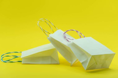 Sarı arka planda izole edilmiş renkli kağıt alışveriş torbaları. Beyaz alışveriş torbalarının yakın çekimi.