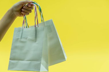 İzole edilmiş sarı arka planda bir sürü farklı renkli boş alışveriş torbası tutan çocuk eli görüntüsü. Kara Cuma indirim konsepti. Boşluğu kopyala, kapat.