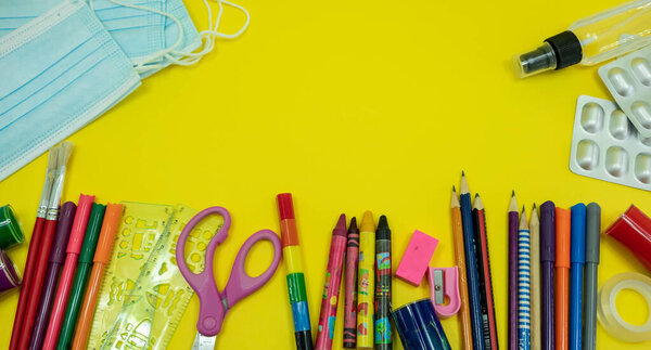 School supplies like pencil scissor eraser ruler watercolor mask alcohol sanitizer on yellow background. Back to school concept during covid pandemic with copy space