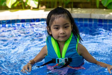 Yüzme dersinde yüzme havuzunda yelek giyerken gülümseyen güzel Asyalı çocuk.