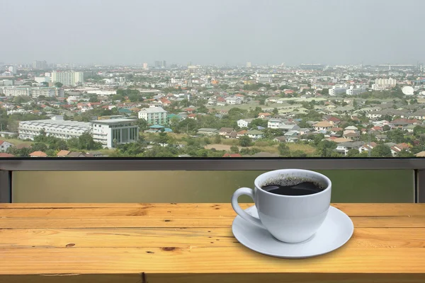 Csésze kávé a fa padló és a kilátás a város háttér — Stock Fotó