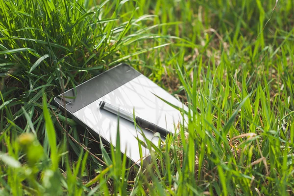Tableta gráfica con un bolígrafo acostado en la espesa hierba de la primavera — Foto de Stock