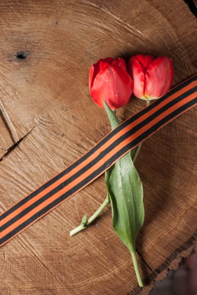 Cinta de San Jorge y tulipanes rojos sobre fondo de madera — Foto de Stock