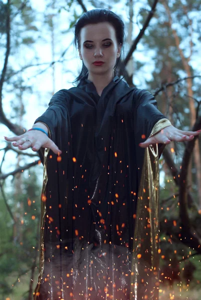 Una joven bruja en el bosque, una mujer con un vestido oscuro sobre un fondo de viejas ramas , — Foto de Stock