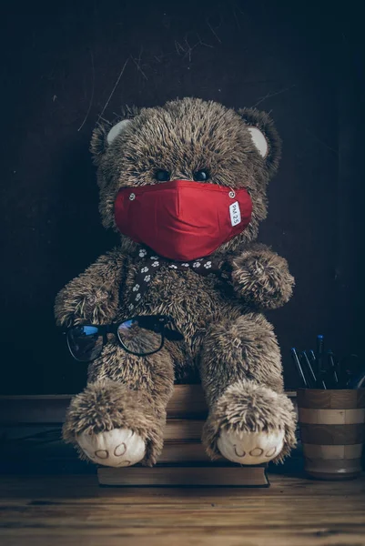 Ένα αρκουδάκι με ιατρική μάσκα κάθεται σε εγχειρίδια στο φόντο ενός πίνακα. — Φωτογραφία Αρχείου