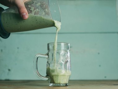 Ahşap arka planda bir bardak sebze püresi. Bir el bardağı doldurur.