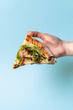 Kadın elinde taze roka ile bir dilim pizza tutuyor. Mavi stüdyo arka planda, yakın çekim, stüdyo çekimi.