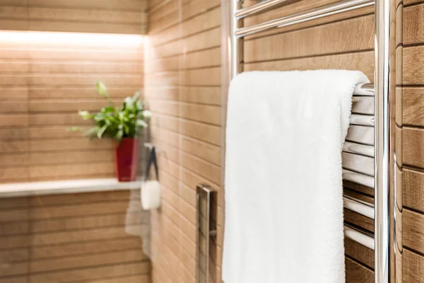 Wooden bathroom interior with heated towel rail and white towel on it.