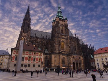 Prag Kalesi 'ndeki Gotik St. Vitus Katedrali. Alacakaranlıkta gökyüzü dramatik bulutlu ve turistlerle dolu.