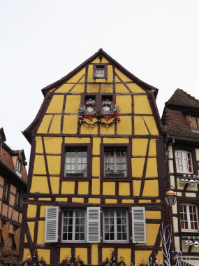 Colmar, Fransa - Aralık 12025: Koyu ahşap kirişli ve beyaz pencereli renkli sarı yarı ahşap bina
