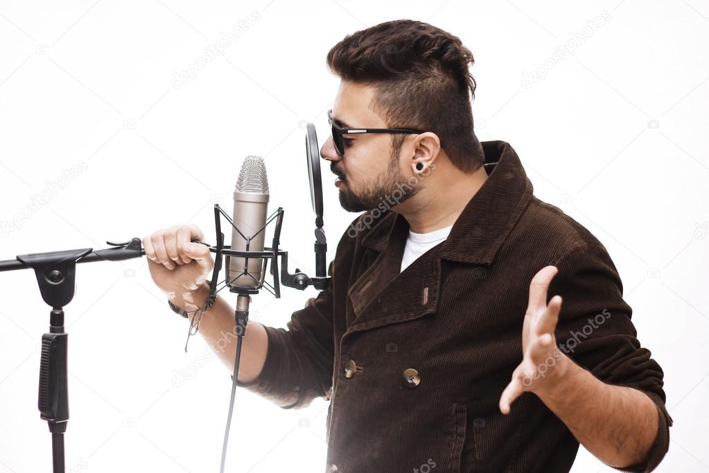 Men brown coat and glasses singing into a condenser microphone