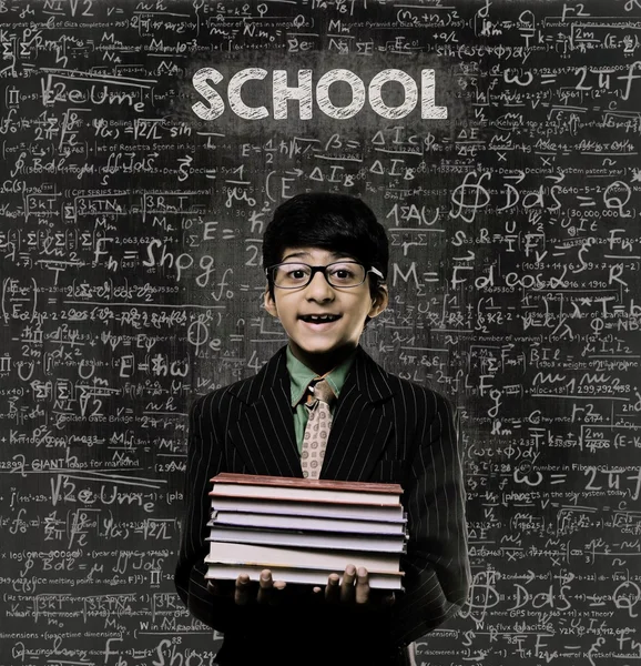 Na escola. Genius Little Boy Segurando Livro vestindo óculos Chalkboar — Fotografia de Stock