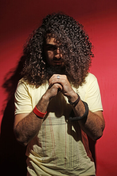 Young guy fashion and long beautiful curly hair against red 