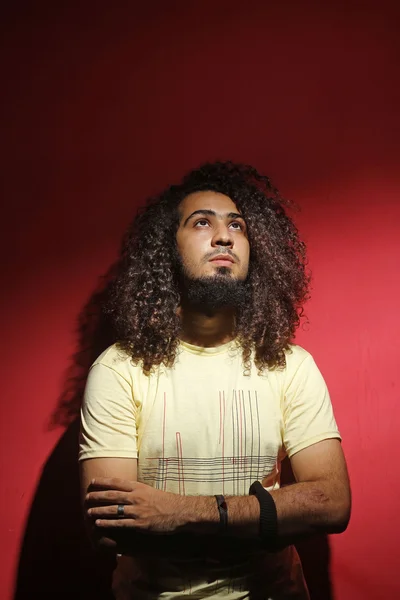 Moda homem e cabelo encaracolado bonito longo contra fundo vermelho — Fotografia de Stock